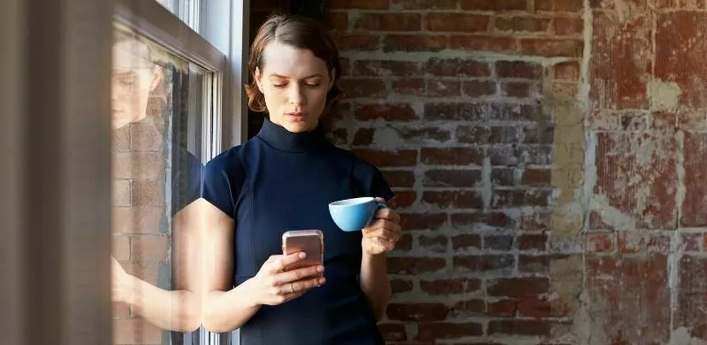 En dame står og ser på telefonen sin. Foto